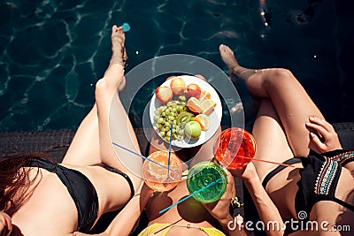 Top view. Girls in swimsuits eat fruits and drink cocktails drinks in swimming pool in summertime. Stock Photo