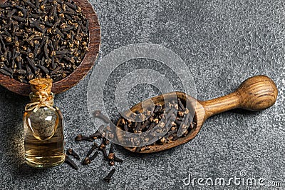 Top view glass bottle of clove oil and cloves in wooden shovel or spoon and bowl on grey rustic table Stock Photo