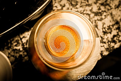 Top view of a glass cup of freshly brewed black espresso coffee with crema and golden foam of fine bubbles on a marble table and Stock Photo