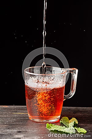 Top view of glass with rooibos tea falling on wooden table with mint leaves, Stock Photo