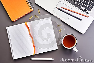 Top view of gray office desk with opened notebook or diary with blank page, cup of tea and laptop. Business concept Stock Photo