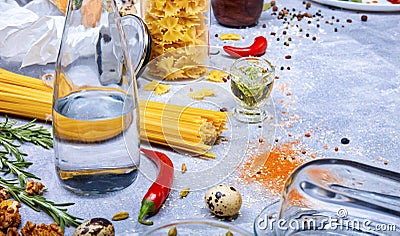 Top view of a gray table with pasta, glass bottle, red chili pepper, quail eggs and walnuts on a gray background. Stock Photo