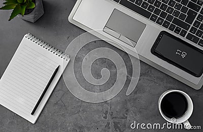 Top view grayscale shot of a laptop, mobile phone, coffee, and notebook on a table Stock Photo