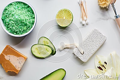 Top view of green bath salts, soap and pumice stone near fresh flower, lime and cucumber on marble surface. Stock Photo