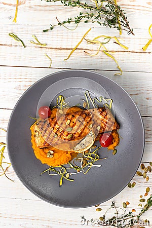 Top view grilled salmon steak with creamy pumpkin puree, fried cherry tomatoes and thyme, lunch menu of national food restaurant Stock Photo