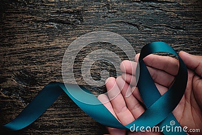 Top view of hand holding teal ribbon on dark background with copy space. Cervical and ovarian cancer, sexual assault, pcos, ptsd Stock Photo