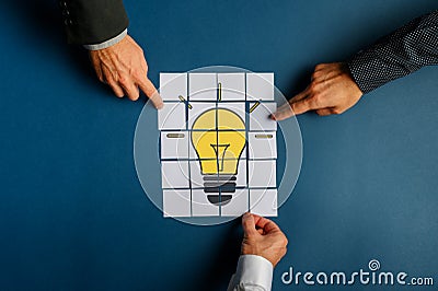 Hands of three businessmen assembling a lightbulb drawn on post it papers Stock Photo