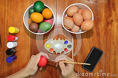 Top view of hands of young christian man is coloring Easter eggs with a paintbrush on wooden table. Stock Photo