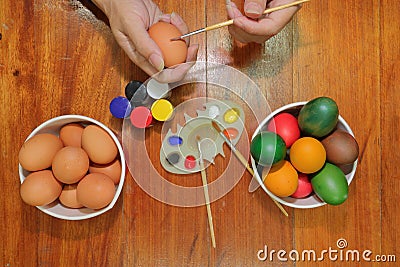 Top view of hands of young people coloring easter eggs with a paintbrush on wooden top. Stock Photo