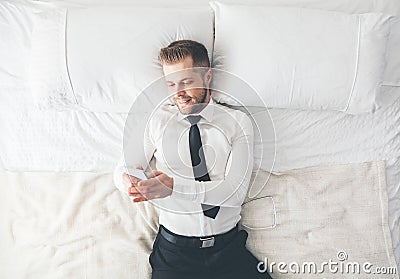 Top view. Handsome businessman lying on bed texting from his smartphone Stock Photo