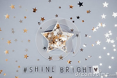 Top view hashtag Shine bright phrase and star shape full of glittering stars confetti on the grey background with shining stars. Stock Photo