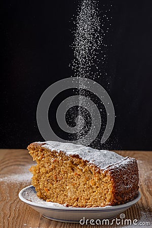 Top view of icing sugar falling on portion of carrot cake, in blue and white plate on wooden table with black background Stock Photo