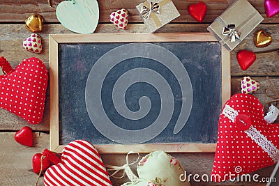 Top view image of colorful heart shape chocolates, fabric hearts, gift boxes and chalk board on wooden table Stock Photo