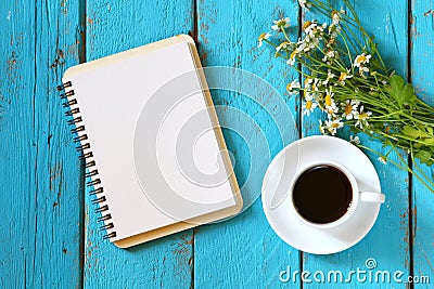 Top view image of daisy flowers, blank notebook next to cup of coffee on blue wooden table. Stock Photo