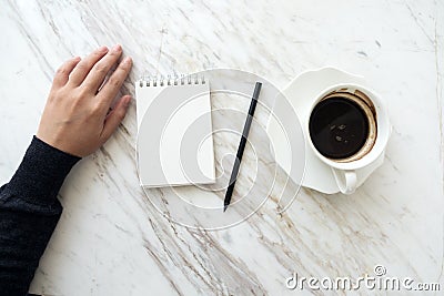 A hand going to write down on a blank white notebook with coffee cup on table Stock Photo