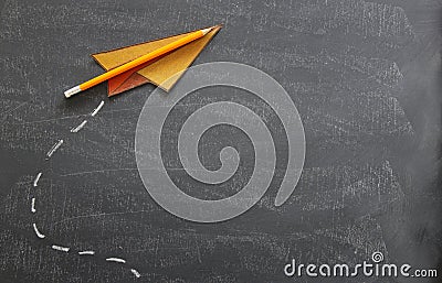 Top view image of paper plane and pencil over classroom blackboard background. Stock Photo