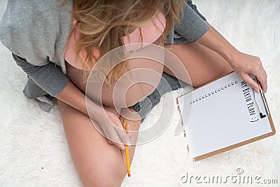 Top view image of pregnant woman holding birth plan checklist and pencil while sitting on her bed at home Stock Photo