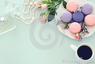 Top view image of white cup of coffee, perfume, white pearls and colorful macaron or macaroon over pastel wooden background. Stock Photo