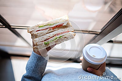 A woman holding and eating whole wheat sandwich and coffee in the morning Stock Photo