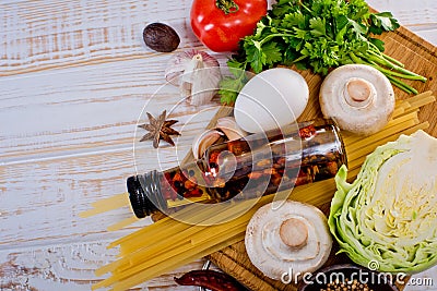 Top view on italian pasta, vegetable, olive oil in bottle, mushrooms, tomatos, egg, parsley, bad, nutmeg, chilli on white wooden. Stock Photo