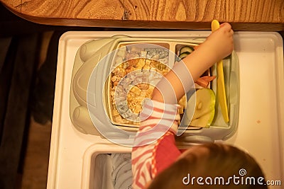 Top view, the kid sits in front of a children`s plate full of delicious mouth-watering food and takes a children`s plastic knife Stock Photo