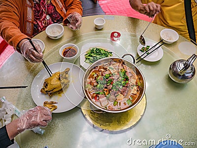 Top view of `Larouguo` or Spicy Smoked pork hotpot and boiled chicken with tourist hand useing chopstick and wear Plastic gloves Stock Photo