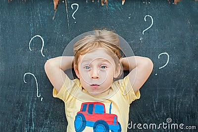 Top view of a little blond kid boy with question mark on blackboard. Concept for confusion, brainstorming and choice Stock Photo