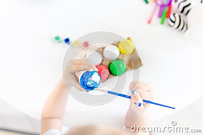 Top view of little girl holding paintbrush and decorating Easter eggs with blue watercolor over white table Stock Photo