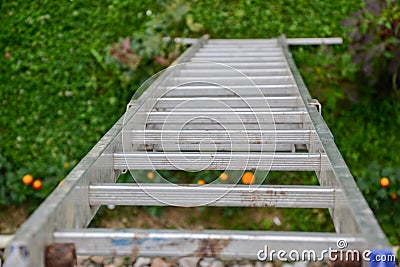 Top view of a long silver aluminum ladder leaning against the wall of the house. Close up view from top of tall step ladder Stock Photo