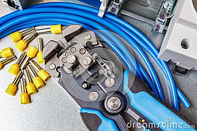 Top view of lying on metal mounting plate wire stripper and blue stranded wire with unused yellow cord end insulated ferrules Stock Photo