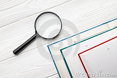 Top view magnifying glass and opened books in different color covers on a white wooden table Stock Photo