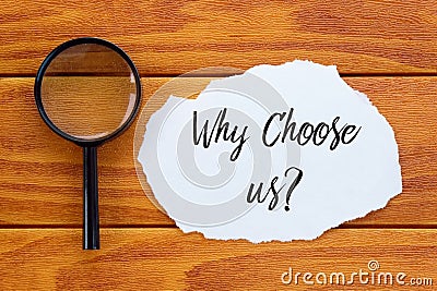 Top view of magnifying glass and piece of paper written with question Why Choose Us? on wooden background. Stock Photo