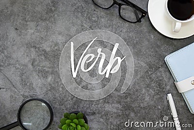 Top view of magnifying glass,plant,pen,notebook,coffee and glasses on grey grunge floor written with Verb Stock Photo