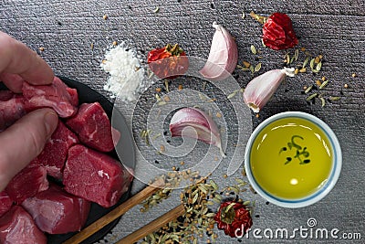Top view of a male hand taking raw cut meat from a table with garlic cloves, dried pepper, oil Stock Photo