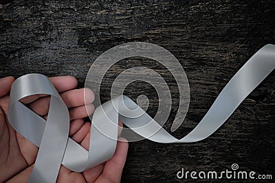 Top view of male hands holding gray ribbon on dark wood background with copy space. Brain cancer tumor awareness concept. Stock Photo