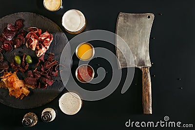 top view of meat knife and gourmet sliced assorted meat on slate board with sauces and spices Stock Photo