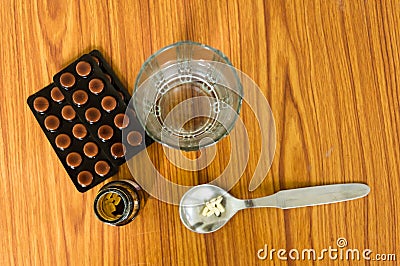 Top view of medicine pills or tablets in spoon, bottles and a glass of water along with a blister pack on wooden table background Stock Photo