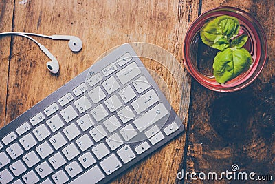 Top view of minimal workspace with computer keyboard, earphones and glass of water with mint leaves on a vintage wooden desk. Editorial Stock Photo