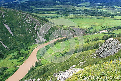 Top view of a mountain landscape with a brown river, blue distance, cliffs, green meadows Stock Photo