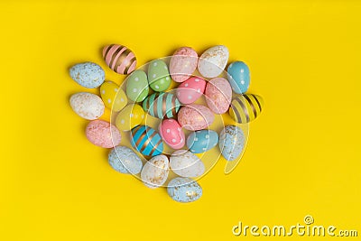 Top view of multicolored festive eggs in shape of heart. Easter eggs on yellow background Stock Photo