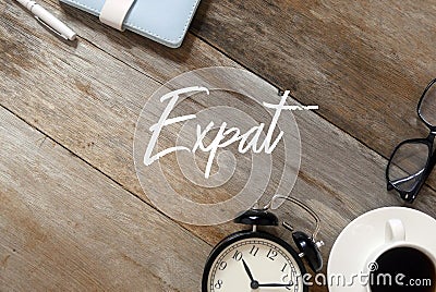 Top view of notebook,pen, clock,a cup of coffee,sunglasses on wooden background written with Expat Stock Photo