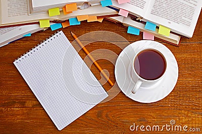 Notebook and pencil with a cup of tea in front of pile of books with bookmarks Stock Photo