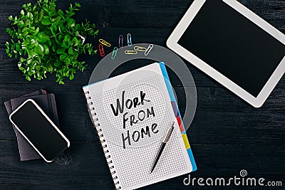Top view of open notebook written with WORK FROM HOME inscription. Green flower, tablet, colored paper clips, smart, pen Stock Photo