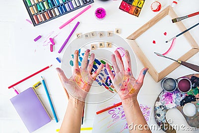 Top view opened painted female hands over Create art words lettering with many colorful paintiing materials on white background. Stock Photo