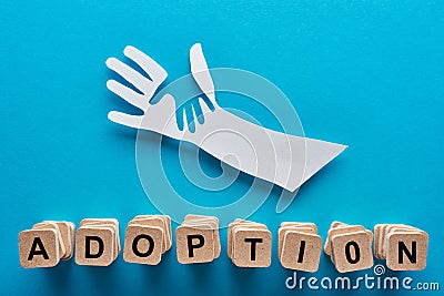 Top view of paper cut parent and child hands and adoption lettering on blue background. Stock Photo