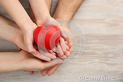 Top view of parents and kid holding red heart in hands at wooden table, space for text. Family day Stock Photo
