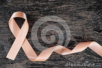 Top view of peach ribbon on dark wood background. Uterine and endometrial cancer awareness concept. Stock Photo