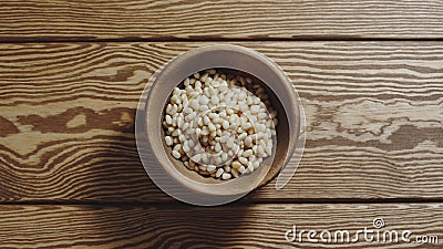 TOP VIEW: Peeled pine nuts fill wooden cup on a wooden table Stock Photo