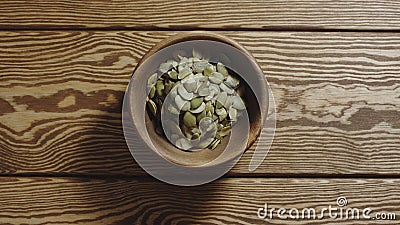 TOP VIEW: Peeled pumpkin seeds fill wooden cup on a wooden table Stock Photo
