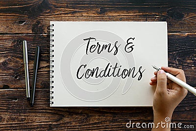 Top view of pen and hand holding pen writing Terms and Conditions on notebook on wooden background Stock Photo